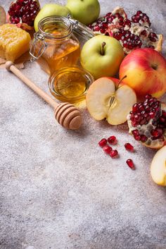 apples, honey, and pomegranates are arranged on a gray surface