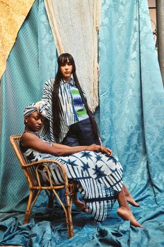 two people sitting on a chair in front of a curtain