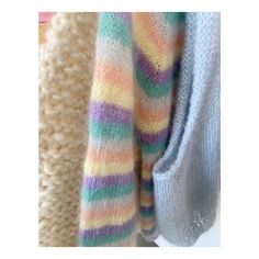 three sweaters hanging up on a rack in front of a white wall and one is multicolored