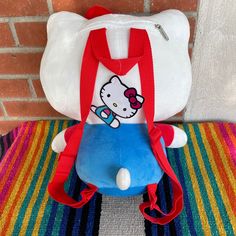 a hello kitty backpack sitting on top of a colorful rug next to a brick wall