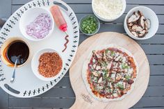 a pizza sitting on top of a wooden cutting board next to bowls of toppings