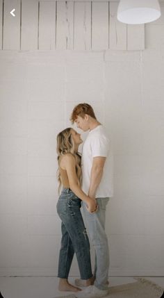 a man and woman standing next to each other in front of a white wall kissing