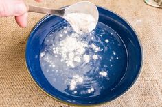 a person spooning sugar into a blue bowl