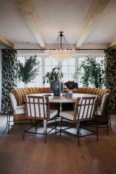 a living room with a round table surrounded by chairs and couches in front of large windows