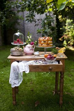 a wooden table topped with cakes and desserts on top of green grass covered ground