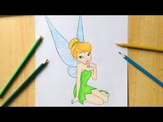 a cartoon tinkerbell sitting on top of a table next to colored pencils