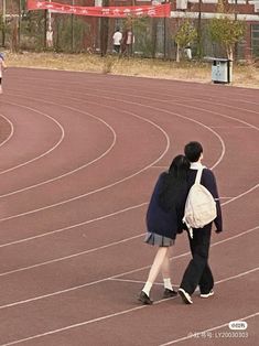 two people are walking on a track in the middle of an empty stadium, one is carrying a backpack