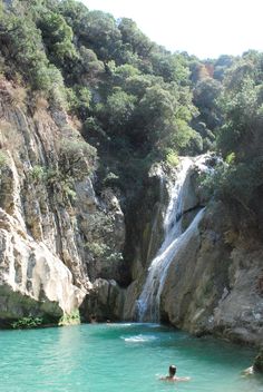 a man swimming in a pool next to a waterfall and some trees on the side