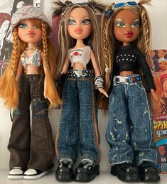 three dolls standing next to each other in front of a wall with posters on it