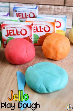 colorful play dough sitting on top of a wooden table next to boxes of jello