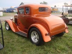 an orange car parked on top of a lush green field next to other cars in the background