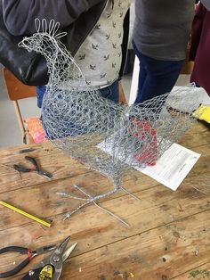 two women are working on wire chicken sculptures with pliers and pencils next to them