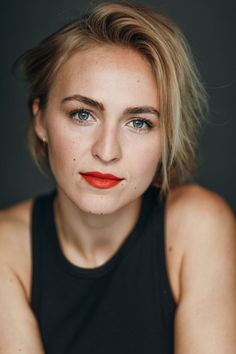 a woman with blonde hair and blue eyes is posing for a studio photo in black tank top