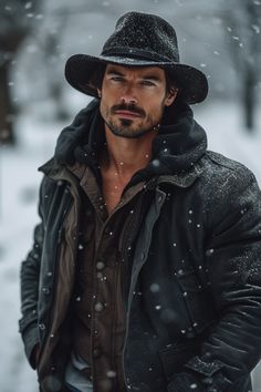 a man wearing a black hat and jacket standing in the snow with his hands on his hips