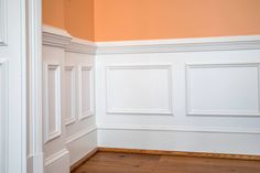 an empty room with white paneling and wood floors