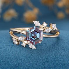 two gold rings with an assorted colored stone and diamond accents on blue surface next to flowers