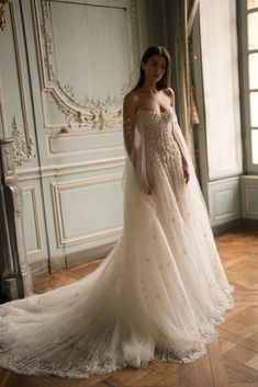 a woman in a wedding dress standing on a wooden floor with an ornate wall behind her