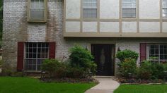 a large brick house with red shutters and green grass in front of the door