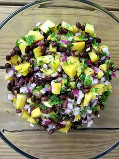 a glass bowl filled with black beans, pineapples and cilantro on top of a wooden table