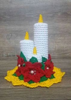 two crocheted candles are sitting on a yellow doily with red flowers and green leaves