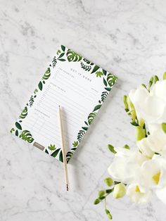 a notepad sitting on top of a marble table next to flowers and a pencil