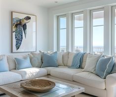 a living room with white couches and blue throw pillows on the coffee table in front of large windows