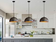 three lights hanging over a kitchen island with marble counter tops and white cabinets in the background