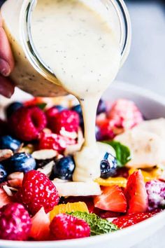 someone pouring dressing over a fruit salad in a bowl