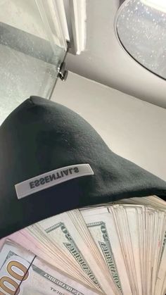 a black hat sitting on top of a pile of money next to a fan of hundred dollar bills