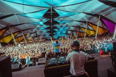 a man standing in front of a large crowd at a music festival with dj's