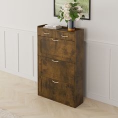 a wooden cabinet with three drawers in front of a white wall and flowers on top