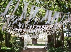 an outdoor wedding ceremony with paper streamers hanging from the trees and white chairs on the ground