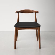 a wooden chair with black leather seat and backrest, in front of a white wall