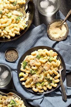 two black plates filled with pasta and broccoli on top of a blue towel