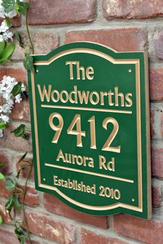 a green and gold sign on a brick wall with white flowers in the foreground