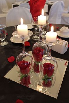 a table topped with wine glasses filled with red roses and floating candles for valentine's day