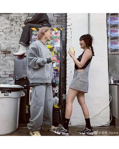 two people standing next to each other in front of a vending machine and talking