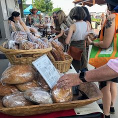 people standing around at an outdoor market with breads and pastries on display in baskets