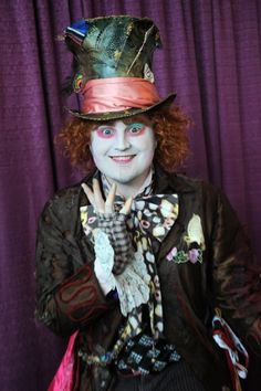 a man with red hair wearing a top hat and holding his hand up to the camera