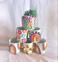 a stack of ceramic pots with plants and rainbows painted on the sides, sitting on a white surface