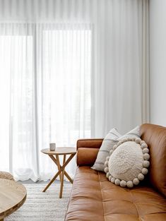 a brown leather couch sitting in front of a wooden coffee table next to a window