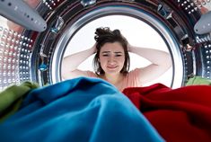 a woman standing in front of a washing machine with her hands on her head and looking at the camera