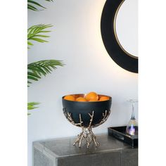 a black bowl filled with oranges sitting on top of a table next to a mirror