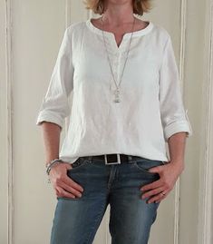 a woman standing in front of a white wall with her hands on her hips, wearing jeans and a white shirt