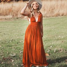 a woman in an orange dress and hat posing for the camera with her hand on her head