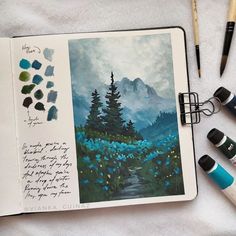 an open notebook with watercolors and pens on it next to some other art supplies