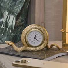 a gold snake clock sitting on top of a desk next to a pen and phone