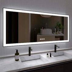 a bathroom vanity with two sinks and a large mirror above it that has lights on