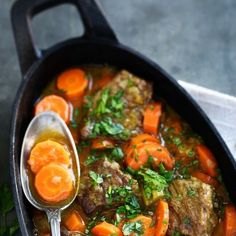 a pot filled with meat and carrots on top of a table next to a spoon