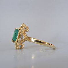 a gold ring with an emerald stone and diamonds on the side, sitting on a white surface